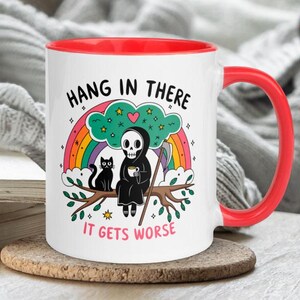Pu&ograve; includere: Tazza da caff&egrave; in ceramica bianca con bordo e manico rossi. La tazza presenta un'immagine di cartone animato della Morte seduta su un ramo con un gatto nero. Il testo sulla tazza recita "Hang in there it gets worse".