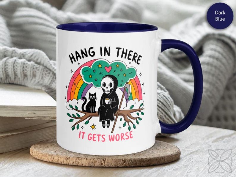 Pu&ograve; includere: Tazza da caff&egrave; bianca con bordo e manico blu. La tazza presenta un'immagine di un cartone animato di uno scheletro che tiene una tazza di caff&egrave; e un gatto nero seduto su un ramo. Il testo sulla tazza dice "Hang in there it gets worse".