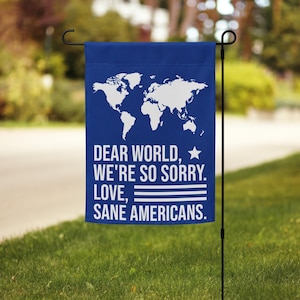 May include: Blue garden flag with a white outline of a world map and the text "Dear World, We're So Sorry. Love, Sane Americans."