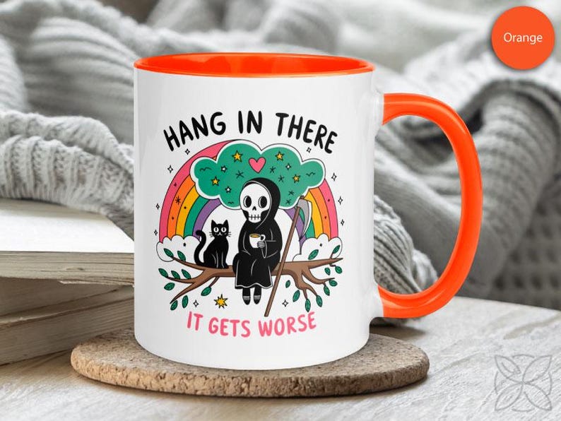 Pu&ograve; includere: Una tazza da caff&egrave; in ceramica bianca con un bordo arancione. La tazza presenta un'illustrazione in bianco e nero di uno scheletro che tiene una tazza di caff&egrave;, seduto su un ramo con un gatto nero. Il testo sulla tazza dice "Hang in there, it gets worse".