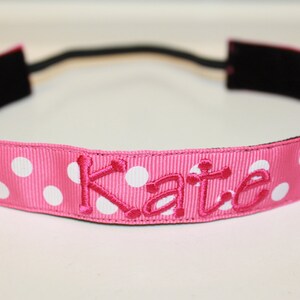 K&ouml;nnte beinhalten: Ein rosa Stirnband mit wei&szlig;en Punkten und dem Namen "Kate" in rosa gestickt.
