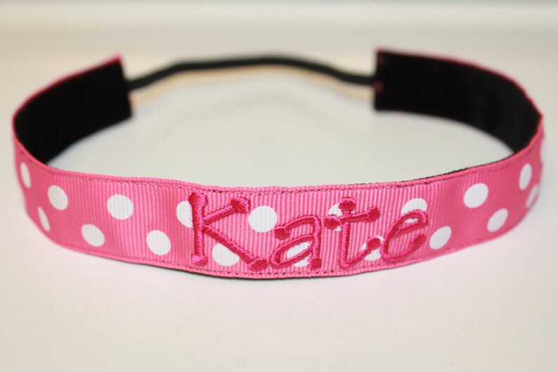 K&ouml;nnte beinhalten: Ein rosa Stirnband mit wei&szlig;en Punkten und dem Namen "Kate" in rosa gestickt.