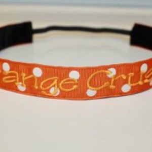 K&ouml;nnte beinhalten: Orangefarbenes Stirnband mit wei&szlig;en Punkten und dem in Gold gestickten Text "Orange Crush".