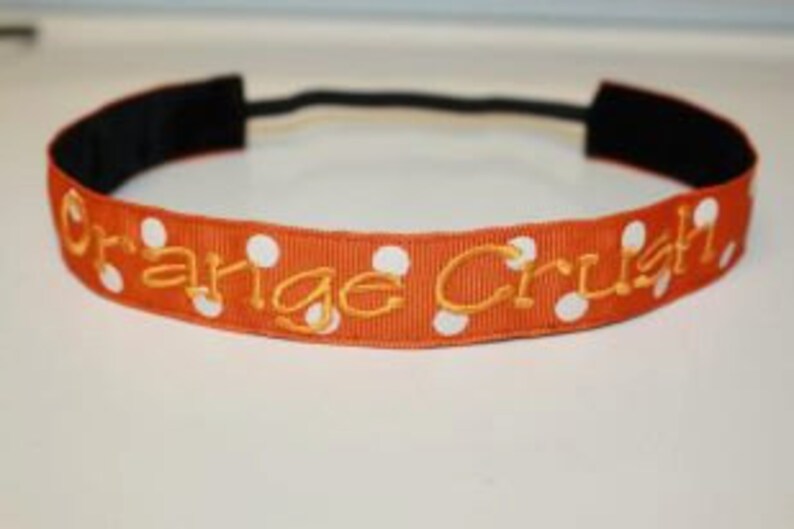 K&ouml;nnte beinhalten: Orangefarbenes Stirnband mit wei&szlig;en Punkten und dem in Gold gestickten Text "Orange Crush".