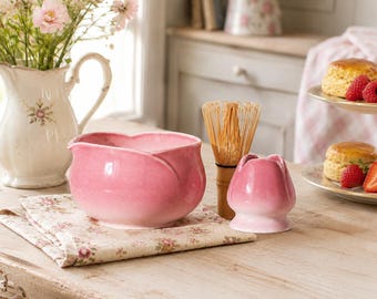 May include: A pink ceramic matcha bowl with a petal-like rim, a bamboo matcha whisk, and a matching pink ceramic whisk holder. The bowl and holder feature a gradient finish, transitioning from a deeper pink at the top to a lighter shade at the base.
