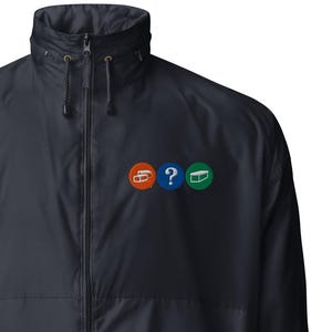 May include: A navy blue windbreaker jacket with a zipper closure and a small embroidered design on the left chest. The design features three circles with different colors and symbols.