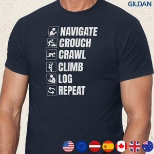 May include: Navy blue t-shirt with white text and icons. The text reads "NAVIGATE, CROUCH, CRAWL, CLIMB, LOG, REPEAT" with corresponding stick figure icons. The Gildan logo is visible in the upper right corner.
