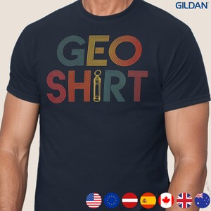 以下が含まれることがあります： レトロなスタイルの「GEO SHIRT」の文字が入ったネイビーブルーのTシャツ。「GEO」の文字はオレンジ、黄色、青で、「SHIRT」は赤と緑で書かれています。単語の間には、黄色のツールのイラストがあります。