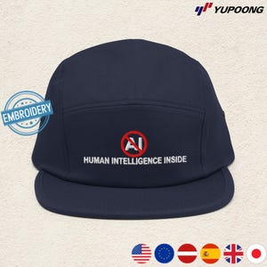 May include: Navy blue five-panel cap with a flat brim. The cap features white embroidered text that reads "HUMAN INTELLIGENCE INSIDE" below a red circle with a crossed-out "AI" symbol. The cap has a "EMBROIDERY" patch.