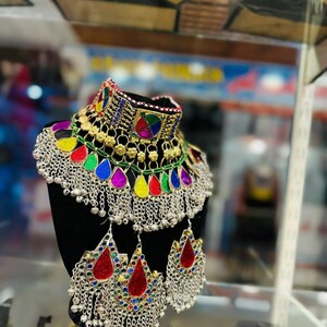 May include: A colorful silver and gold necklace with dangling charms and red, green, blue, and purple accents. The necklace is displayed on a black mannequin bust.