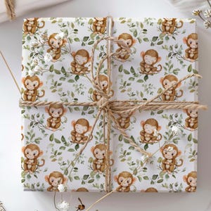 May include: A wrapped gift with white wrapping paper featuring a repeating pattern of cartoon monkeys and green leaves. The gift is tied with natural twine and accented with sprigs of white flowers.
