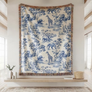 May include: A large, rectangular throw blanket with a blue and white toile pattern featuring elephants, giraffes, and trees. The blanket has a fringed edge and is displayed on a wall. The overall theme is safari or wildlife.