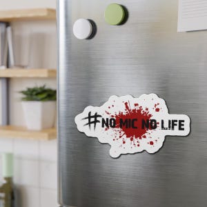 May include: A white magnet with the text "#NO MIC NO LIFE" in black, with a red splatter design in the center. The magnet is rectangular with rounded edges and is displayed on a silver refrigerator.