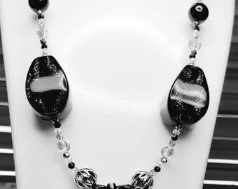 May include: A black and silver necklace with a teardrop-shaped pendant. The necklace features black and silver beads, as well as a black and silver tassel.