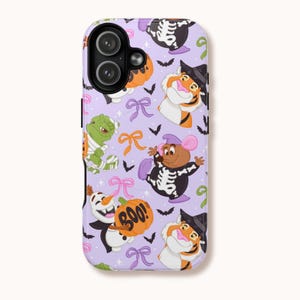 Puede incluir: Una funda de teléfono lila con un diseño de Halloween. El diseño incluye personajes de dibujos animados disfrazados, como una momia, un esqueleto y una bruja. La funda también tiene murciélagos, lazos y una calabaza con la palabra "BOO!"