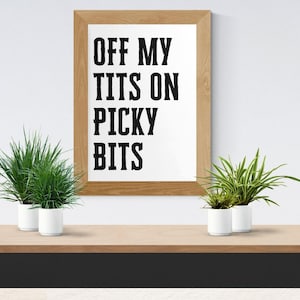 Könnte beinhalten: Ein gerahmter Druck mit dem Text "OFF MY TITS ON PICKY BITS" in fetten schwarzen Buchstaben. Der Rahmen ist hellbraun. Zwei kleine Topfpflanzen mit grünem Laub stehen auf einem Holzregal.