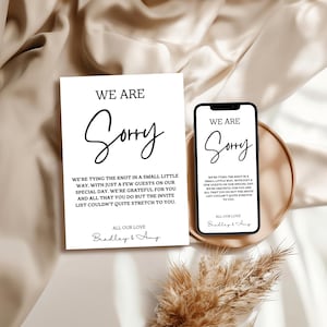 May include: A white card and a smartphone display the text "WE ARE Sorry" in elegant script. The card and phone share the same message: "We're tying the knot in a small little way..." The card is signed "Bradley & Amy."