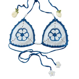 May include: A blue and white crocheted bikini top with floral details and pineapple charms. The top has adjustable straps and ties at the back.