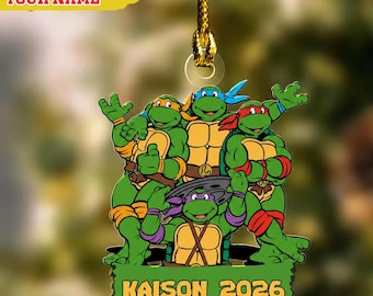 May include: A decorative hanging ornament featuring four green cartoon turtles with colored masks. Below the turtles, a green banner displays the text KAISON 2026 in yellow. The ornament is suspended by a gold cord and includes a custom name area.