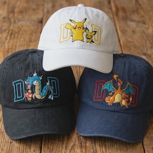 May include: Three baseball caps with embroidered designs. One white cap features Pikachu and Pichu with the word "DAD". A black cap has a blue and red dragon design with "DAD". A navy cap displays a Charizard design with "DAD".