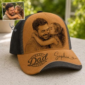 Può includere: Un cappellino da baseball marrone e nero con una foto di un padre e un bambino. Il testo "BEST Dad EVER" e il nome "Sophia" sono stampati sul cappellino.