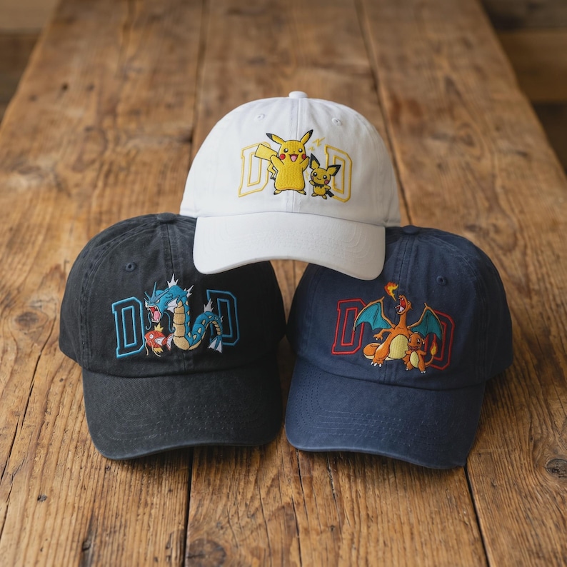 May include: Three baseball caps with embroidered designs. One white cap features Pikachu and Pichu with the word "DAD". A black cap has a blue and red dragon design with "DAD". A navy cap displays a Charizard design with "DAD".