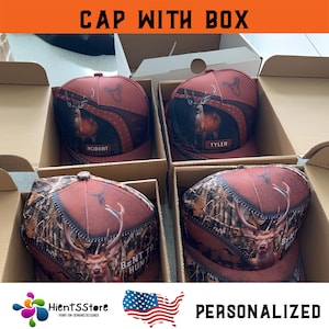 May include: Four personalized baseball caps in boxes. The caps feature a deer graphic with the text "BENT TO HUNT" and names like "ROBERT" and "TYLER". The caps have a camouflage and brown color scheme.