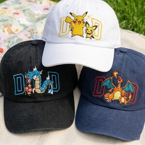 May include: Three baseball caps with embroidered designs. One white cap features Pikachu and Pichu with the word "DAD" in yellow. A black cap has a blue and white dragon design with "DAD". A navy cap displays Charizard and Charmander with "DAD".