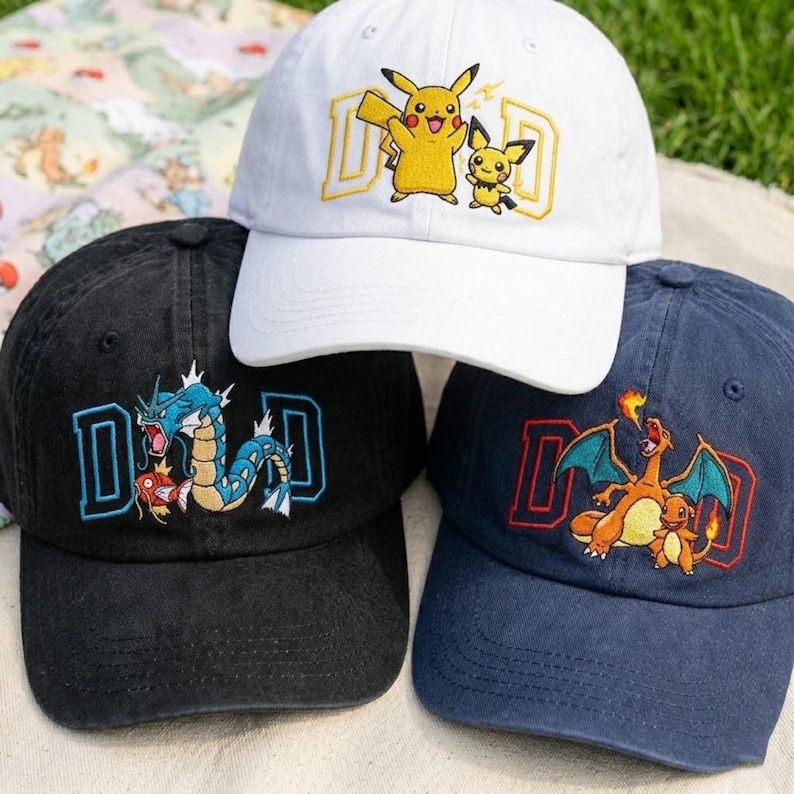 May include: Three baseball caps with embroidered designs. One white cap features Pikachu and Pichu with the word "DAD" in yellow. A black cap has a blue and white dragon design with "DAD". A navy cap displays Charizard and Charmander with "DAD".