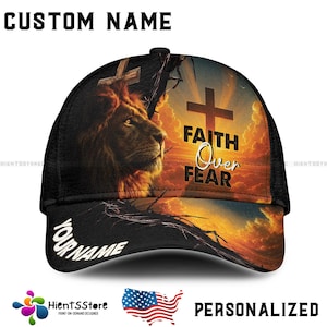 May include: Black baseball cap featuring a lion's face, a cross, and the text "FAITH Over FEAR" against a sunset backdrop. The cap includes the text "YOUR NAME" on the brim and "CUSTOM NAME" on top.