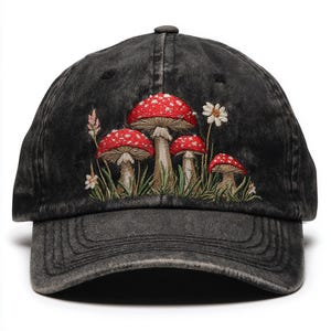 May include: Black denim baseball cap featuring an embroidered design of red and white spotted mushrooms, green grass, and white flowers. The cap has a curved peak and an adjustable strap.