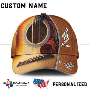 Op de afbeelding: Een bruine baseballpet met een ritsdetail en een gitaarmotief. De gitaar is bruin en heeft een wit klankgat. De pet heeft een bruine klep en een bruine band. De pet heeft de tekst "Name" aan de zijkant.