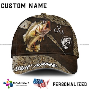 Op de afbeelding: Een bruine baseballpet met een camouflagepatroon met een vis en haken. De pet heeft een gepersonaliseerde naam op de voorkant.