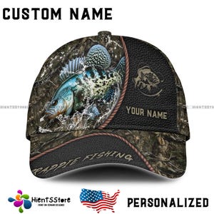 May include: A personalized baseball cap with a camouflage pattern and a crappie fish design. The cap features the text "CUSTOM NAME" at the top and "YOUR NAME" on the side. The words "RAPPIE FISHING" are also visible. The cap is a print-on-demand design.