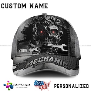 Könnte beinhalten: Eine schwarze und graue Baseballkappe mit einem Schädel- und Zahnrad-Design. Die Kappe trägt den Text "CUSTOM NAME" und "MECHANIC". Der Schädel hat rote Augen und einen Schraubenschlüssel im Mund.