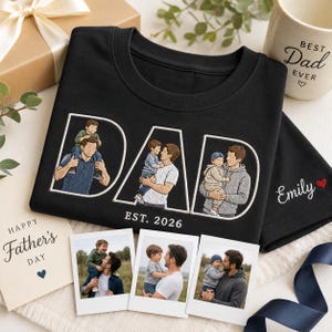 Puede incluir: Camiseta negra con dise&ntilde;o bordado "DAD" con retratos familiares y "EST. 2026". Tambi&eacute;n hay una taza con el texto "Best Dad Ever" y una tarjeta del D&iacute;a del Padre. Incluye tres impresiones fotogr&aacute;ficas y una caja de regalo.