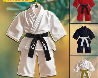 May include: White karate uniform ornament with a black belt. The belt is personalized with the name "DAVID" and the year "2025". Additional karate uniform ornaments in red, black, and white with different colored belts are also shown.