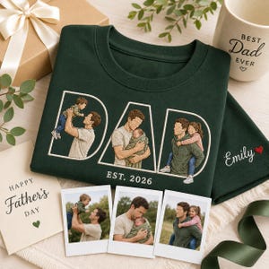 Puede incluir: Una sudadera verde oscuro con la palabra "DAD" bordada en blanco, con im&aacute;genes de un padre con sus hijos. El texto "EST. 2026" est&aacute; debajo de la palabra "DAD". Se ve una taza con "Best Dad Ever".