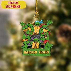 May include: A green ornament featuring the Teenage Mutant Ninja Turtles. The ornament has a gold string for hanging and includes the text "KAISON 2025" on a green banner. The top of the ornament has the text "CUSTOM YOUR NAME" on a yellow banner.