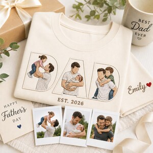 Puede incluir: Sudadera color crema con la palabra "DAD" bordada con ilustraciones de un padre con sus hijos. El texto "EST. 2026" est&aacute; debajo de la palabra "DAD". Una taza con el texto "BEST Dad EVER", una tarjeta que dice "Happy Father's Day" y fotos tambi&eacute;n est&aacute;n en la imagen.