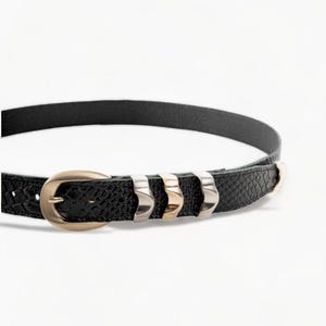 May include: A black leather belt with a gold buckle and silver accents. The belt has a textured surface and is decorated with small metal studs.