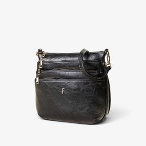 Puede incluir: Un bolso bandolera negro con acabado texturizado, que cuenta con múltiples compartimentos horizontales con cremallera, herrajes de metal dorado y un pequeño emblema metálico con la letra F centrado en el panel frontal con correa ajustable.