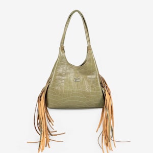 Op de afbeelding: Een groene handtas van imitatieleer met franjes. De tas heeft één bovenste handvat en een klein metalen logo met de tekst "Genuine".