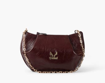 May include: A burgundy leather handbag with a gold chain strap and a gold logo that says "Gemmi".