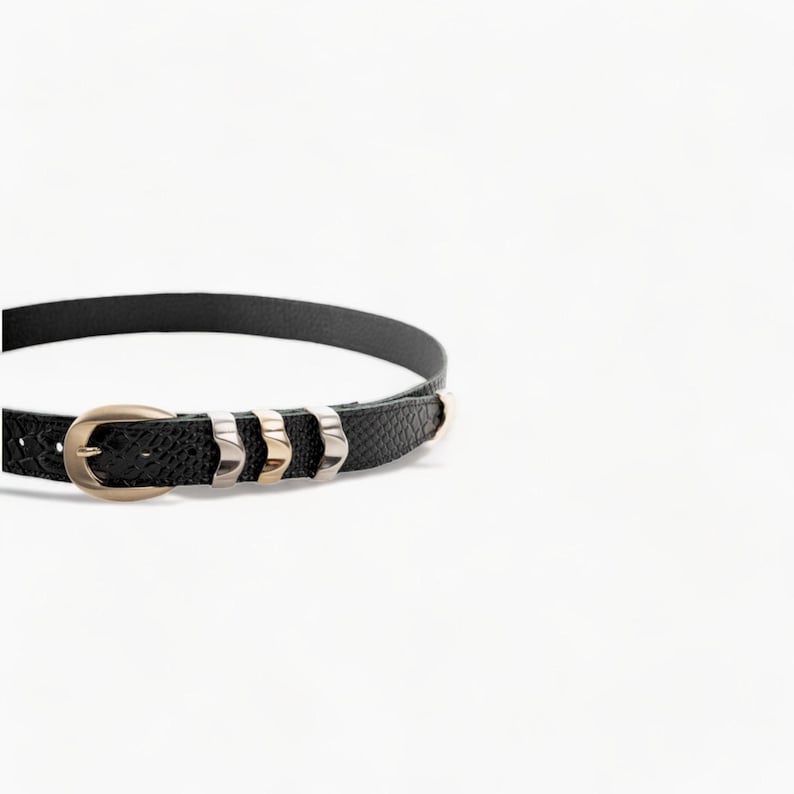 May include: A black leather belt with a gold buckle and silver accents. The belt has a textured surface and is decorated with small metal studs.