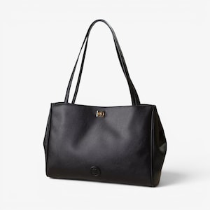 May include: A black tote bag with a textured surface, featuring two long shoulder straps, a gold-toned rectangular turn-lock closure at the top center, and a small circular black emblem centered near the bottom edge of the bag.