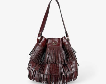 May include: A burgundy leather bucket bag with a tiered fringe design. The bag features a long, thin strap and a small logo on the front. The bag is a deep reddish-brown color.