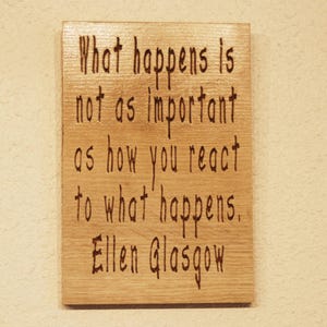 May include: A rectangular wooden plaque with the quote "What happens is not as important as how you react to what happens. Ellen Glasgow" etched into the wood. The wood has a light brown color.