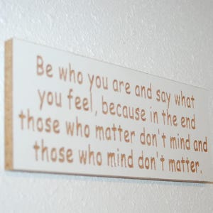 May include: A rectangular wooden sign with the quote "Be who you are and say what you feel, because in the end those who matter don't mind and those who mind don't matter" in brown lettering.