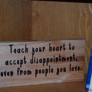 May include: A wooden sign with black text that reads "Teach your heart to accept disappointment, even from people you love."